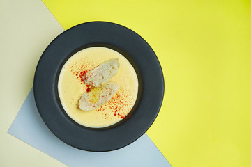 Cheese cream soup in a black bowl with crackers, fried bread and spicies. Tasty food for lunch. colored background