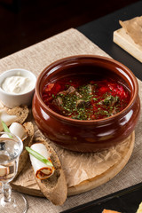 Red beetroot soup borshch in clay pot with bread toast and sour cream on the table at restaurant