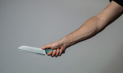 Male hand holds a big sharp knife on a gray wall background
