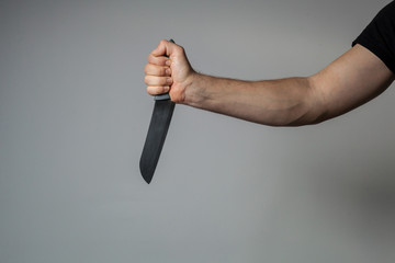 Male hand holds a big sharp knife on a gray wall background