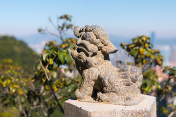 Beautiful Lion stone statue close up. Lion's Pavilion (The Peak), Hong Kong, China. Sunny day with the city's skyscrapers in the background (blurred)