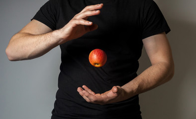 Red apple flying from one hand to another man in black football against gray wall background