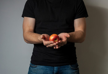 A man in a black t-shirt holds a red apple in front of his chest against a gray wall background