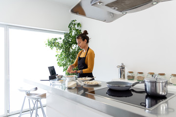 Brunette woman cooking a recipe from a digital tablet in a modern kitchen