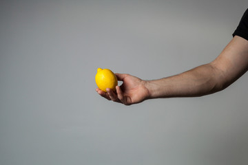 Male hand holding whole lemon on gray wall background