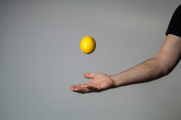 A man's hand throws a whole lemon into the air against a gray wall background