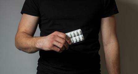 Male build on a white background in a black t-shirt holds a plate of pills in his right hand