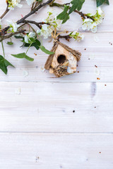 White table top with white spring flowers on a branch with green leaves. Little wooden bird house with wooden bird. Spring time flat lay.