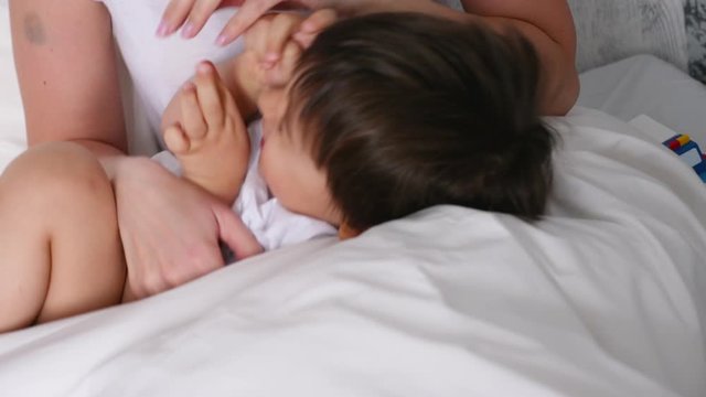 mom tickles her little son lying on the bed
