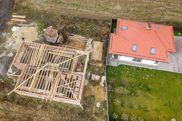 Top down aerial view of two private houses, one under construction with wooden roofing frame and...