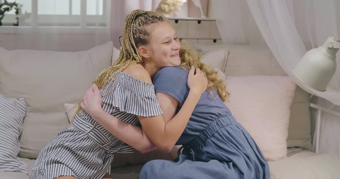 Mother and adult daughter embrace sitting on sofa at home. Loving mom with grown-up child tender relationships