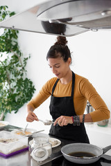 Young brunette woman with an apron cooking homemade croquettes in a modern kitchen