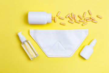Sanitizer, protective mask and pills on a yellow background