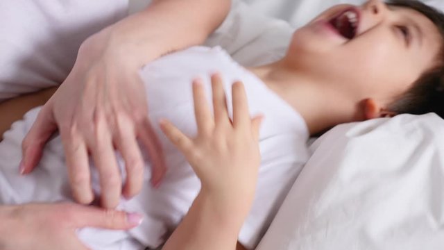mom tickles her little son lying on the bed