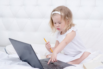 A little girl is engaged in distance learning using a laptop at home in the bedroom. Distance Learning during Quarantine Concept