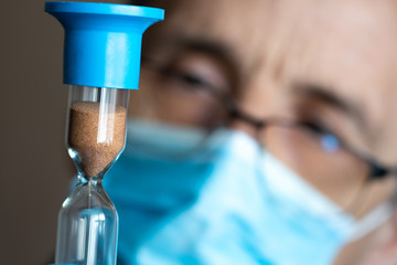 Tired doctor with glasses and mask looks at the hourglass.