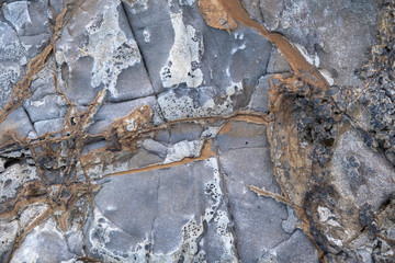 Gray rough stone rock surface with orange and brown splashes.