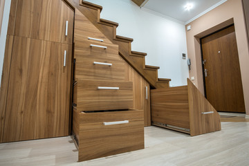 Modern architecture interior with luxury hallway with glossy wooden stairs in multi-storey house. Custom built pullout cabinets on glides in slots under stairs. Use of space for storage.