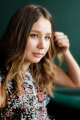Young girl in a floral dress stands on a background of green wall