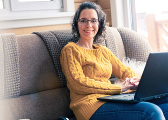 A woman works with a laptop and sits on a sofa in the house