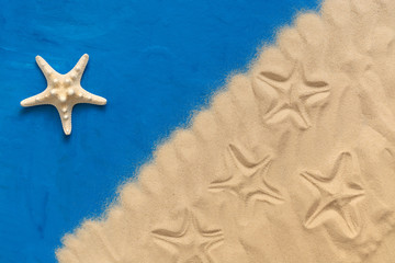 Fototapeta na wymiar Creative composition of sea sand and starfish on a blue painted background. The concept of summer vacation and relaxation. Top view, flat lay, corner frame.