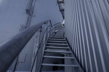 part of the metal industrial tanks outdoor. roof of technological building at the industrial plant on background. Equipment and appliances at the gas company. metal ladder stairs on the tank