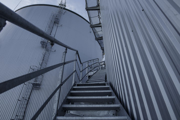 part of the metal industrial tanks outdoor. roof of technological building at the industrial plant on background. Equipment and appliances at the gas company. metal ladder stairs on the tank