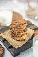 Oatmeal raisins on paper and a wooden stand with milk vertical arrangement