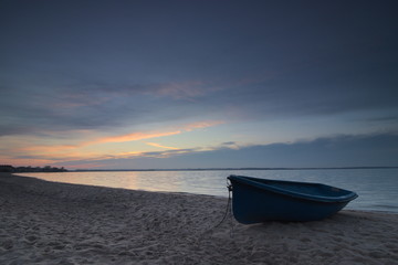 A boat on the beach during sunset.