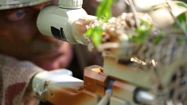 close-up. Soldier looking through sniper scope. Ghillie suit. Tracking the enemy