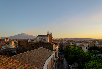 Obraz premium Catania, Sicily in Italy. Aerial view of the city roofs at sunset with the incredible Etna vulcano smoking in the background, nice warm colors and soft light.