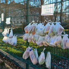 Berlin fence of donations, supporting people in need in the time of the corona virus wih many plastic bags full of vegetables and food gifts by a sign with the message stay social writtten on it.