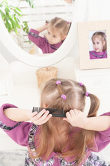 a little three-year-old girl combs herself in front of a mirror
