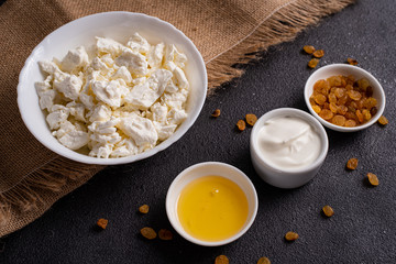 Cottage cheese in a white plate, separately honey, raisins on burlap, a dark background.  Top view.