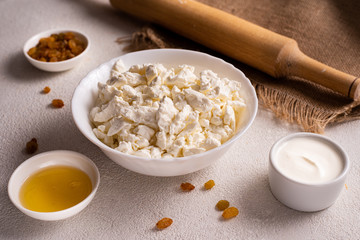 Cottage cheese in a white plate, separately honey, raisins on a white background. Healthy food, close-up.