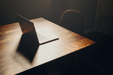 A laptop on wooden table in dark area with leather chair.