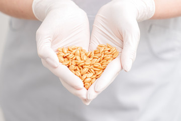 Hard wax beans in palms of cosmetologist's hands close up.
