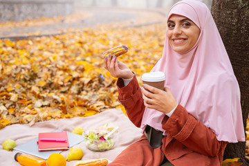 Happy Muslim lady eating eclair and drinking coffee stock photo