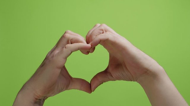 Hands make heart symbol on green background