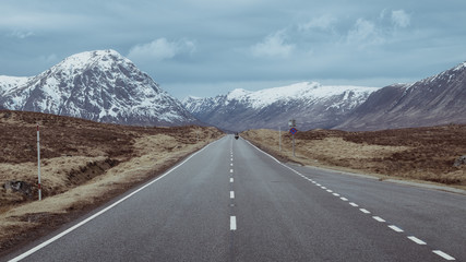 A road leading through the Scottish Highlands of Glen Coe, snowcapped mountains and valley. Scotland - obrazy, fototapety, plakaty