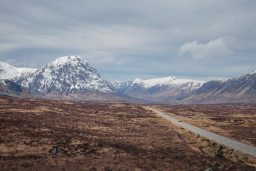 Fototapeta premium A road leading through the Scottish Highlands of Glen Coe, snowcapped mountains and valley. Scotland