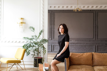 Woman in a black dress sits on the back of a sofa in the interior