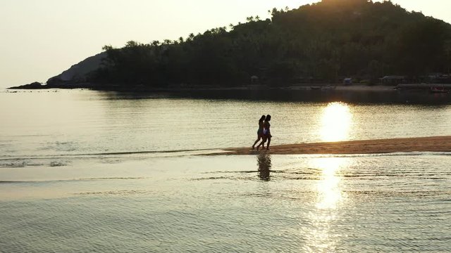 Silhouette of young women walking on sandy stripe surrounded by calm lagoon water reflecting hills of tropical island in Vietnam