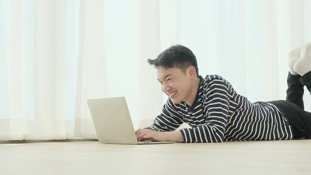 happiness peaceful smile asian male enjoy work from home quarantine  relax and positive work with laptop,asian male attractive smart freelance lay down use laptop on laminate wooden floor