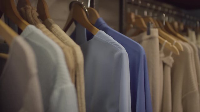Close up tracking shot of stylish garments on hangers hanging on clothes rack at boutique
