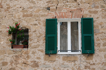 Fototapeta na wymiar A window with green shutters and a window with potted flowers against a tuff wall