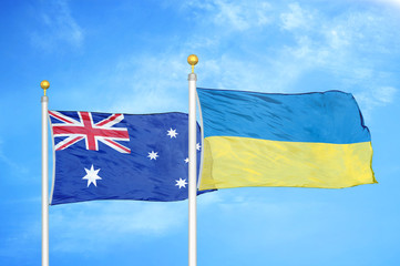 Australia and Ukraine two flags on flagpoles and blue cloudy sky