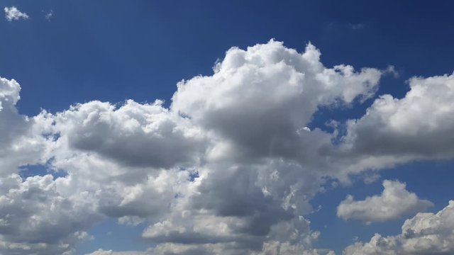 Blue summer sky with dense thick rain clouds moving across the heavens. Fast cloud formation and movement creating a surreal time lapse.