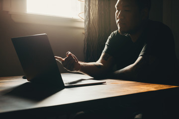  A asian man working  on laptop in dark area. Pointing to the screen.