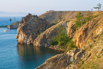 The rocky coast of Olkhon island on a summer evening in the rays of the setting sun. Pleasure boat in the blue waters of Lake Baikal.